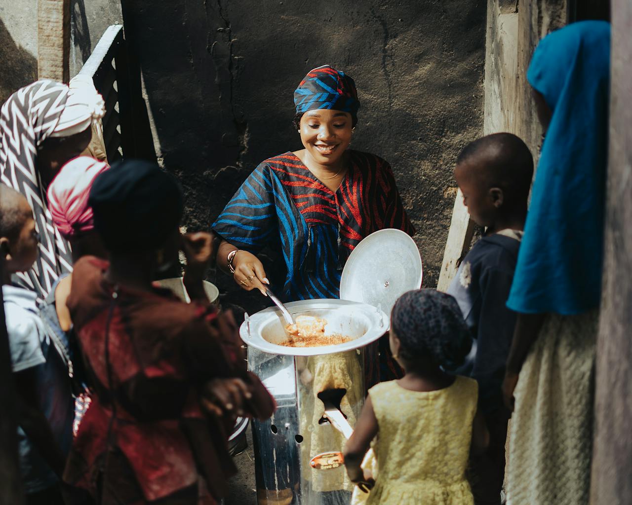 Mastering the First Impression: Your intriguing post title goes here A woman serves food from a large pot to a group of children outdoors in an African community.