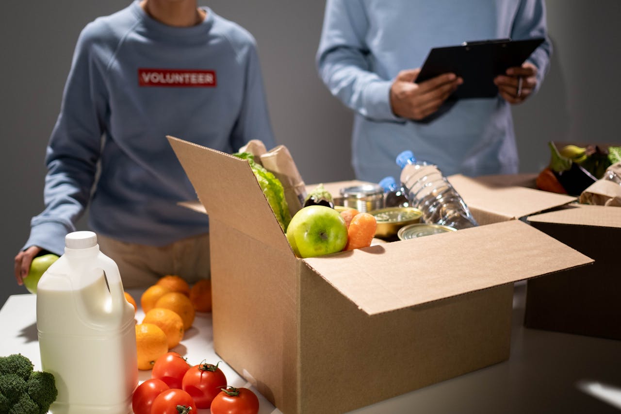 Eko Akete People packing a cardboard box with essentials like fruits, vegetables, and bottled water for charity.