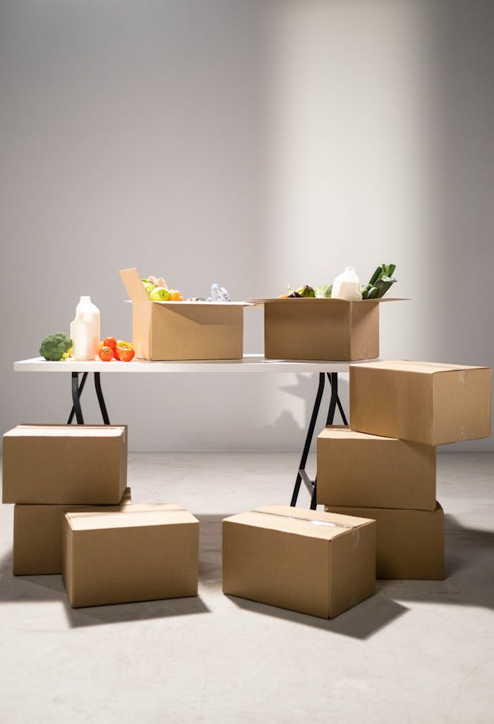 Eko Akete Cardboard boxes filled with assorted groceries on a white folding table indoors.