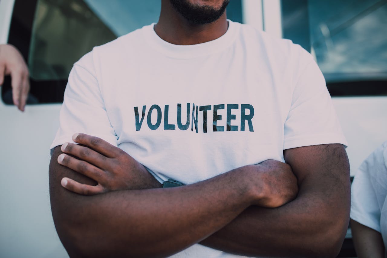 Crafting Captivating Headlines: Your awesome post title goes here A close-up of a person wearing a volunteer shirt with arms crossed, promoting community service.